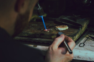 Jeweler soldering on work bench a gold ring with flame from welding torch in an authentic jewelry...