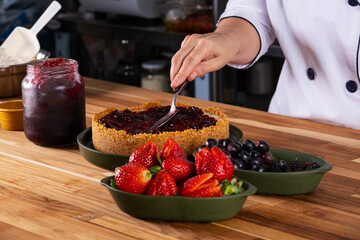 hand with spoon spreading berry jam on sweet pie