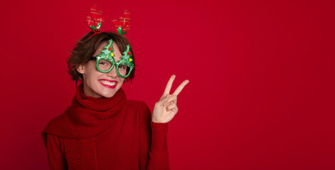 Funny attractive young lady in Christmas reindeer horns and glasses is posing and enjoying on party...
