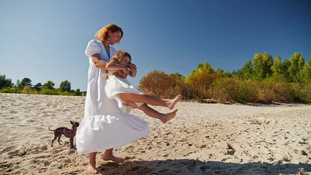 Mom spinning with her daughter and laughing on the sandy beach