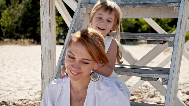 Mom and daughter in white dresses spend time together on the beach and have fun