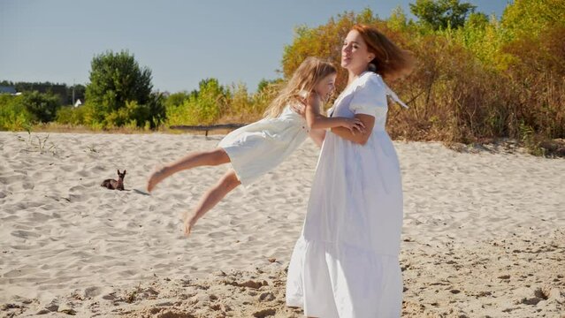 Mom spinning with her daughter and have fan on the sandy beach