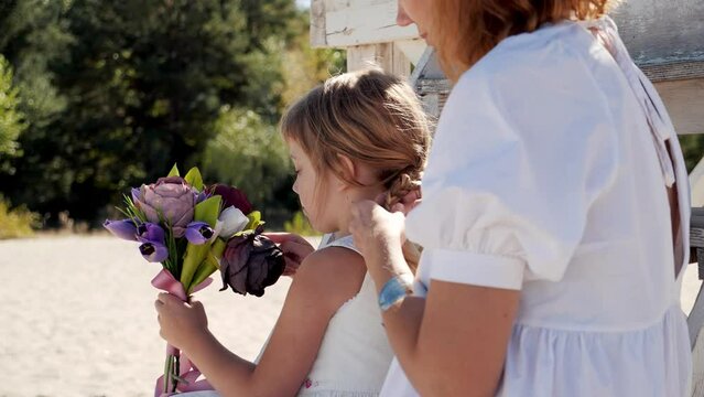 Mom and daughter in white dresses spend time together on the beach and have fun