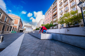 In Madrid's streets, a bearded man prepares for dynamic parkour maneuvers.