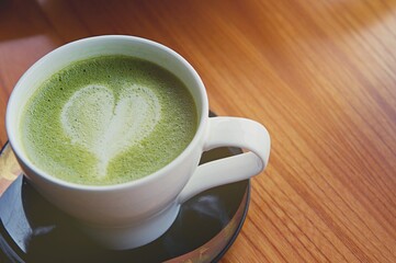 Matcha latte art heart shape on top on wooden table with some green tea powder beside and tools for tea making, Japanese style