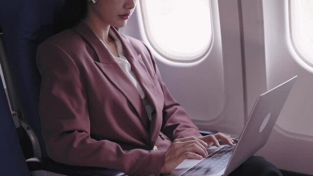 An Asian businesswoman is working on her laptop, actively recording and analyzing tasks during her flight. She is dedicated to maximizing productivity while in transit
