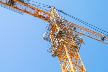 The tower construction crane is orange against the blue sky. Rotary boom of the tower crane. Construction in the city. There are workers on the steel construction of the crane. © Eduard Belkin