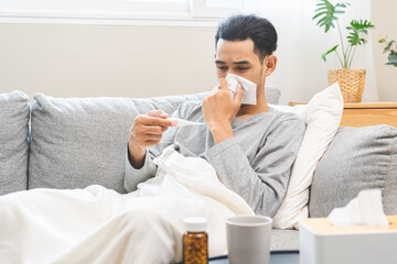 Sick, influenza asian young man have fever blowing nose, sneezing in tissue, holding thermometer...