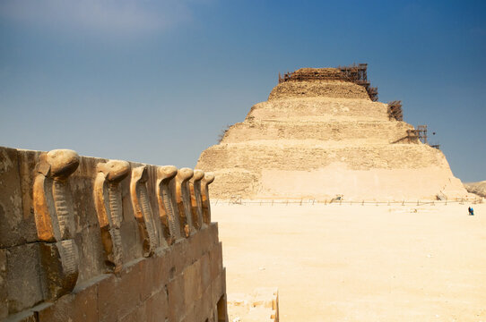 Frieze of cobras with the step pyramid of Saqqarah, south of Cairo, in the background. This pyramid is a creation of Imhotep, architect of Djeser. Snakes are divine symbols of Pharaoh.
