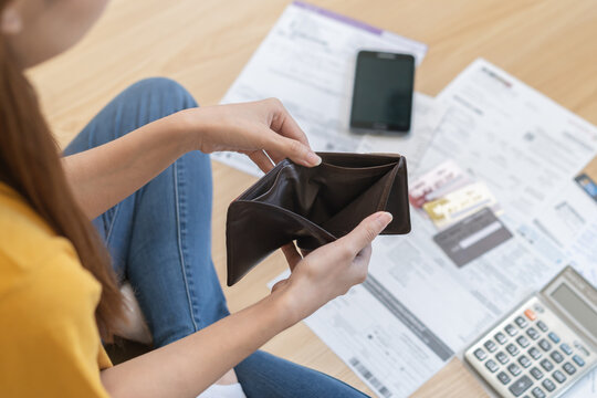 Stressed, problem people asian woman, girl sitting on floor at home, hand holding wallet open empty purse no money to pay bill, loan or expense in payment. Bankruptcy, bankrupt and debt financial.
