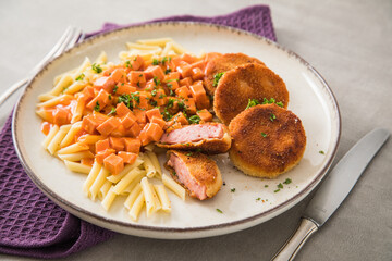 Jägerschnitzel nach DDR GDR Rezept mit Jagdwurst paniert, Makkaroni Penne Nudeln, Tomatensoße, Petersilie mit Teller, Besteck, lila Serviette und Marmor Hintergrund