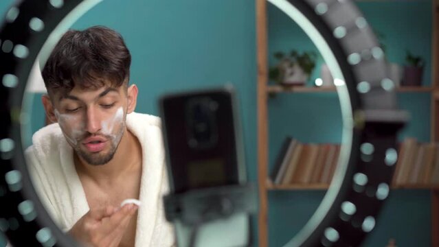 Arabic beauty male blogger filming daily skin care routine tutorial at camera, applying cleanser face foam. Influencer guy livestreaming cosmetics product review at home. Male cosmetic