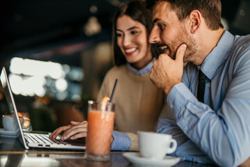 Side view of cheerful couple using a laptop together while sitting in a cafe