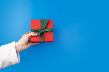 Hand with a gift box on a blue background, Birthday shopping, decorative packaging, happy celebration