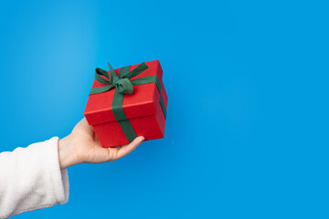 Hand with a gift box on a blue background, Red package, green ribbon, joyful season