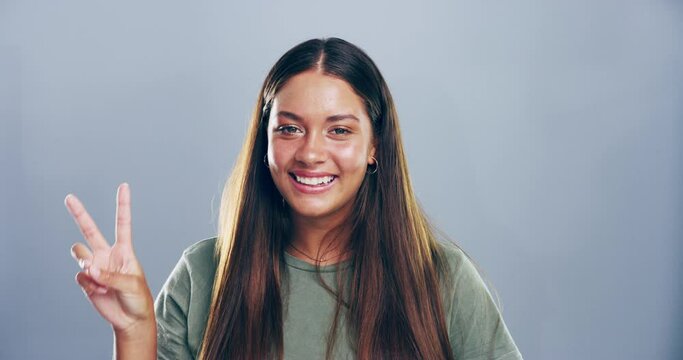 Face, woman and sign of peace in studio for winning, success and vote on grey background. Portrait, happy gen z model and v emoji for victory, hope and icon of feedback, support freedom and pride