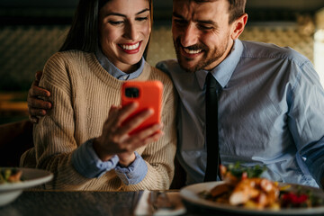 Two smiling people using a phone together while spending time in the restaurant.
