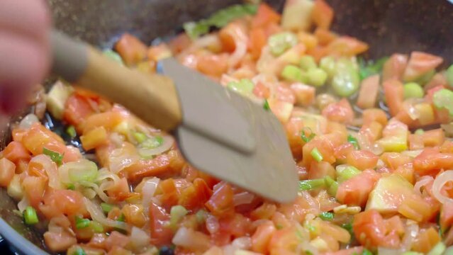 Person cooking healthy eating at home, saltwater fish fillets stewing with fresh chopped tomatoes, garlic, onion and celery in cooking pan, fish pieces rich on omega-3 and other nutrients