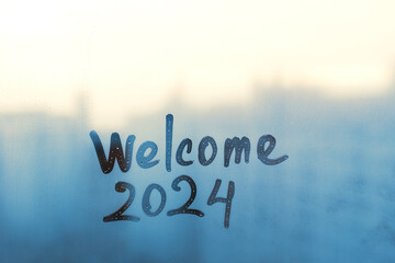 lettering Welcome and numbers 2024 of new year paint with finger on splashed by rain foggy glass on...