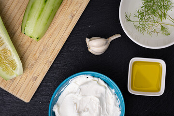 Ingredients for the traditional Bulgarian Snejanka or Mlechna salata flay lay on black background:  cucumbers, garlic cloves, dill herb, olive oil and strained greek yogurt.