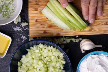 A chef is cutting cucumbers on a chopping board, surrounded by ingredients for the Bulgarian...