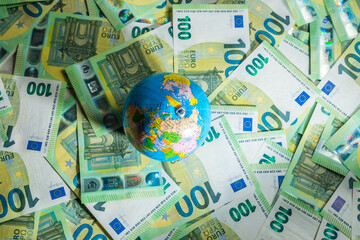 A little round globus over many money bills of 100 euros, top view - obrazy, fototapety, plakaty