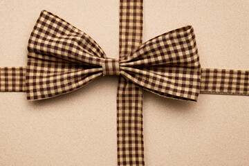 checkered brown bow. fabric texture of light beige color, bow with ribbons, top view. wallpaper background concept