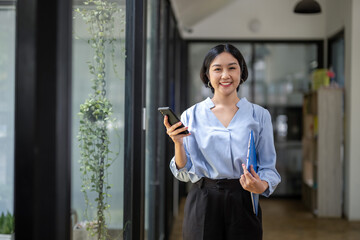 Asian businesswoman stands holding a clipboard and uses the phone to talk about work, calling friends or co-workers. Give advice during working hours.