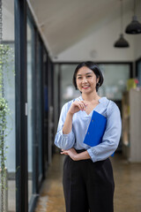 Fototapeta premium Vertical image of standing businesswoman holding a pen and document clipboard under her arm.