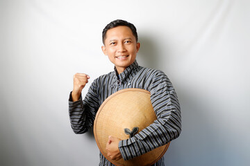 Indonesian farmer wearing Lurik holding a Caping standing with clenched hand isolated on white background.