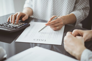 Woman accountant using a calculator and laptop computer while counting taxes for a client. Business...
