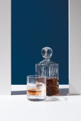 Vaso de whisky con hielo y decantador sobre fondo azul