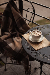 Autumn composition on a cafe table on the street. Plaid and fragrant marshmallow cocoa