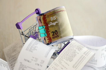 Brazilian reais money bills bunch in shopping trolley surrounded by many paper receipts close up