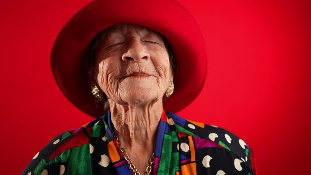 Closeup fisheye view of funny elderly senior woman 80s dreaming of great memories, thinking, wearing red hat isolated on red studio background
