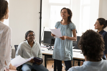 Cheerful happy African American employee speaking on business group meeting, holding report, paper document, laughing, talking to diverse colleagues. Team brainstorming in modern office