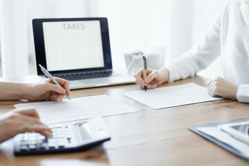 Two accountants using a laptop computer and calculator while counting taxes at wooden desk in office. Teamwork in business audit and finance