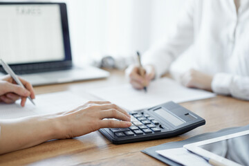 Two accountants using a laptop computer and calculator while counting taxes at wooden desk in office. Teamwork in business audit and finance