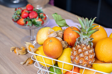 Juicy citrus fruits in a white metal basket, fresh red strawberries in a glass bowl, physalis and a...