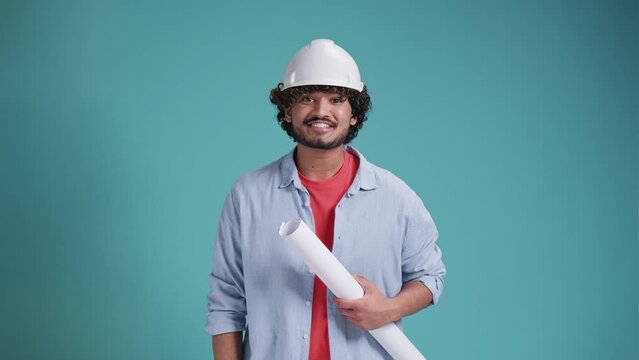 Young Latin engineer standing holding helmet, blueprint and wearing ear muff standing happy delighted isolate on a blue background.
