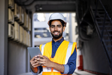 Happy engineer builder in helmet standing near building with tablet in hands, arab work foreman looking and smiling at camera, senior project worker designer leader concept.