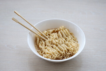 Bowl of instant cooking noodles with wooden chopsticks on white wooden table close up
