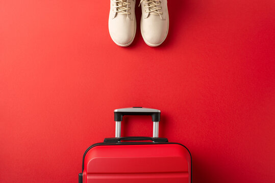 Christmas getaway idea. Overhead shot of white woman's winter boots, signifying the path to a winter vacation, and a suitcase on a red backdrop, with space for your message