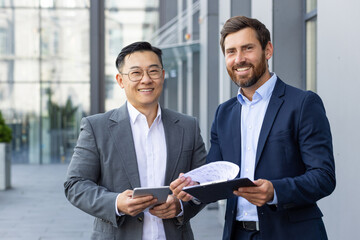 Two happy adult business men in suits standing outside office, discussing important work issues,...