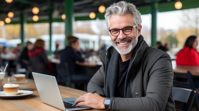 Dedicated elderly man with fashionable eyeglasses intently furthers his tasks on a laptop