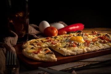 Closeup of a delicious pizza cut in rectangular slices with tomatoes and red peppers beside it