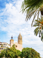 Fototapeta na wymiar Church of St. Bartholomew and Santa Tecla in Sitges, Catalonia, Spain against a background of blue sky, palm trees and plants, vertical photo with copy space