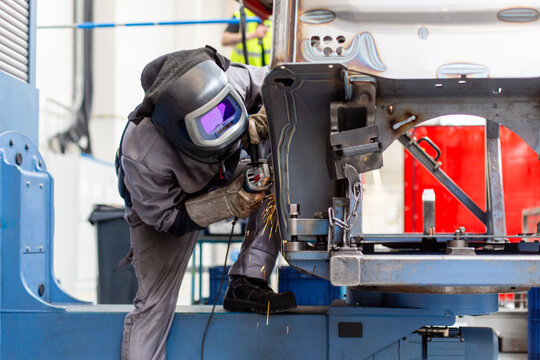 Professioneller Schwei&szlig;er und Metall-Arbeiter in heller Industriehalle in Schutzkleidung schwei&szlig;t und schleift dickes Metall und Stahl mit Funken 