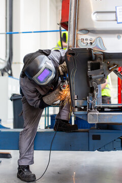 Professioneller Schwei&szlig;er und Metall-Arbeiter in heller Industriehalle in Schutzkleidung schwei&szlig;t und schleift dickes Metall und Stahl mit Funken 