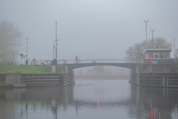 View of the cyclists crossing a drawbridge above the river on a foggy day